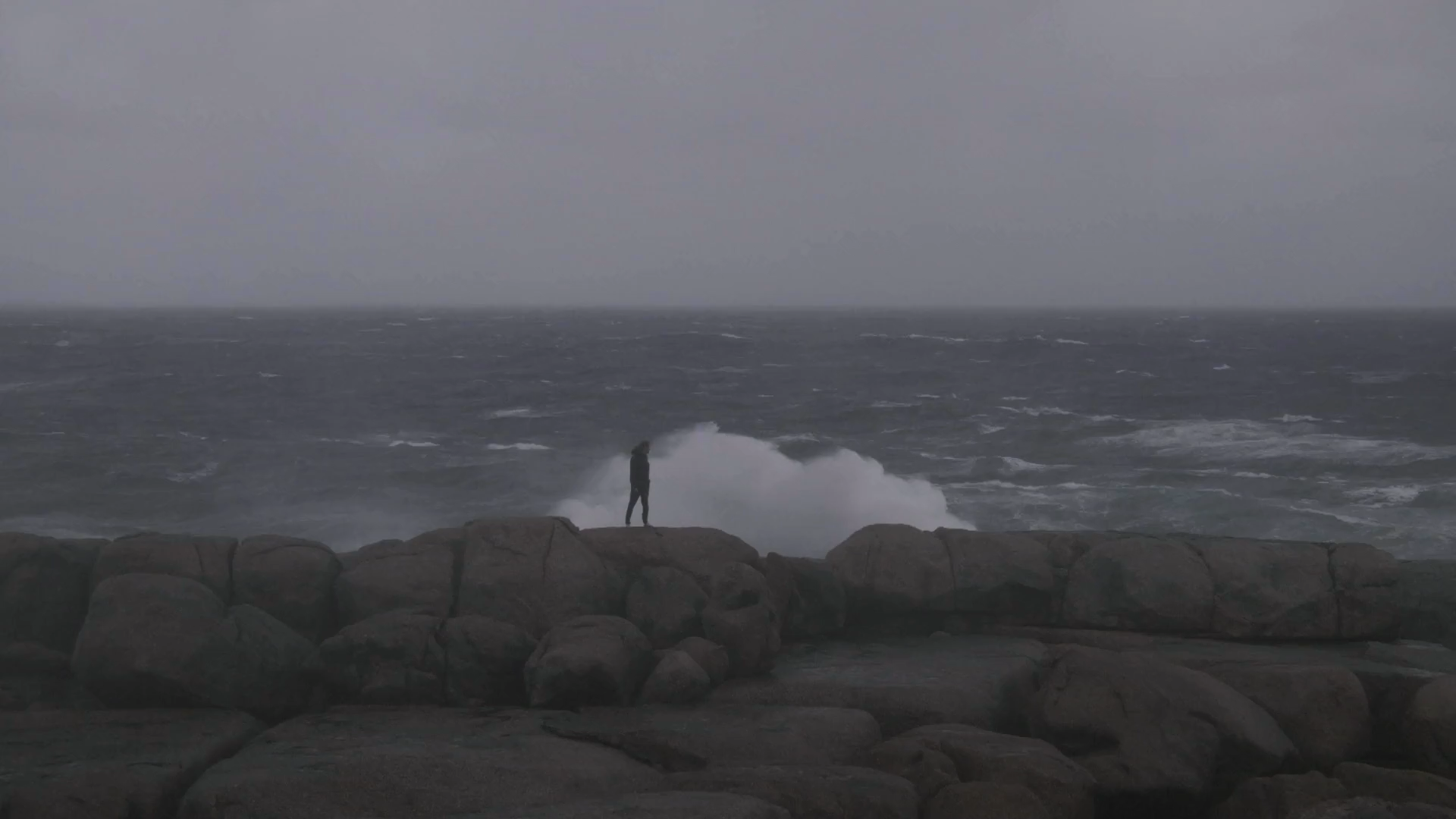 A person on the rocky Norwegian coastline facing breaking waves